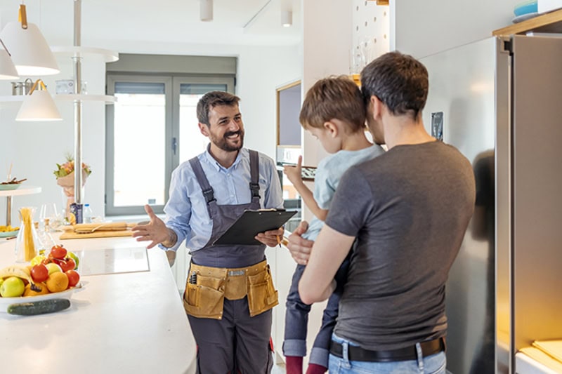 hvac technician in uniform talking to male client and his small son indoors.