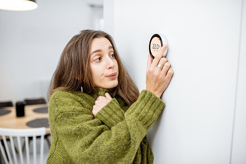 Why Is My Heat Pump Turning On and Off Frequently? A woman turning her heat up.